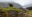 A grizzly bear stands along the rocky shoreline of Khutzeymateen/K’tzim-a-deen Grizzly Sanctuary, with mist-covered coastal temperate rainforest in the background near Prince Rupert.