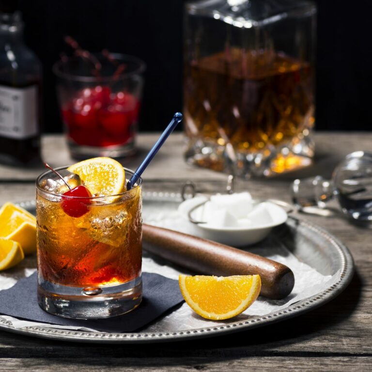 Old Fashioned cocktail garnished with a cherry served on a tray with slices of orange