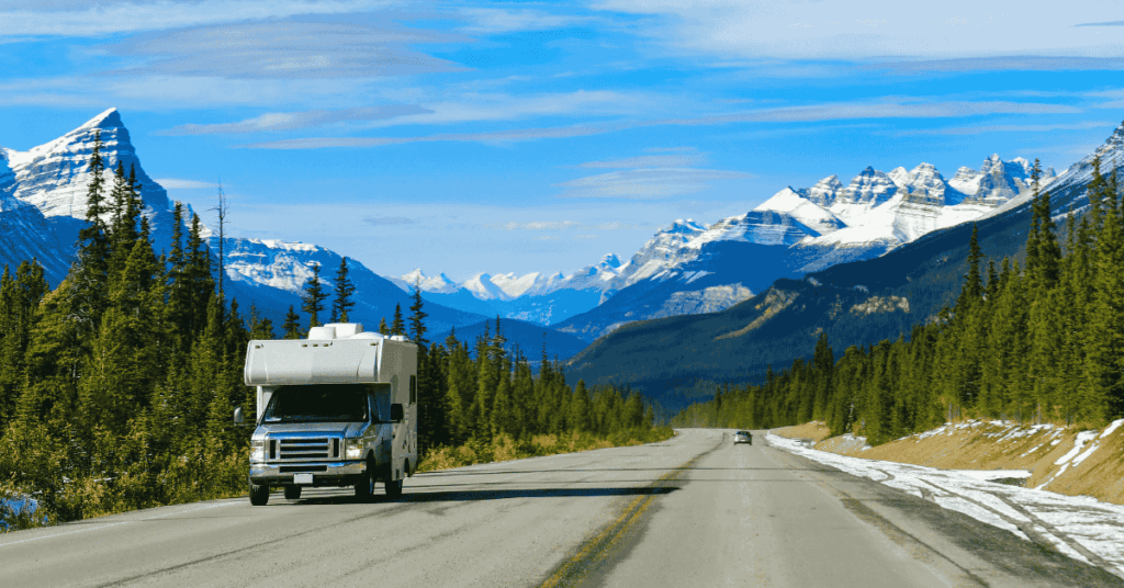 Motorhome driving along a scenic road in Canada, surrounded by lush forests and distant mountains under a bright blue sky