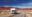 RV driving along a winding road through striking red rock formations in the American Southwest under a clear blue sky.