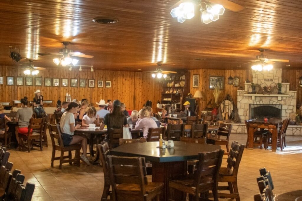 Inside the dining hall at Mayan Dude Ranch in Bandera, Texas, with guests enjoying hearty, family-style meals in a rustic, timber-accented setting.