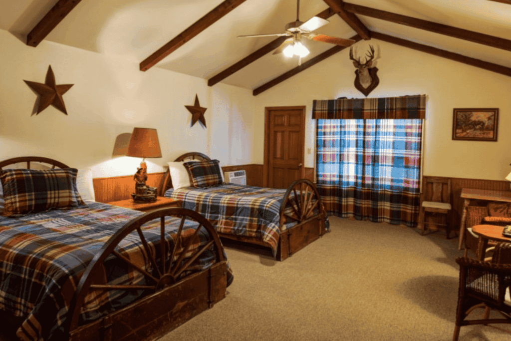 Cozy twin bedroom at Mayan Dude Ranch in Bandera, Texas, featuring rustic timber accents, handmade quilts, and a porch overlooking Hill Country.