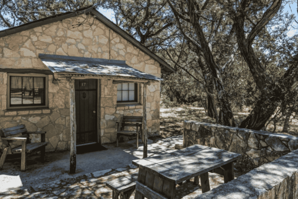 Exterior view of a rustic lodge at Mayan Dude Ranch in Bandera, Texas, surrounded by oak and cedar trees in scenic Hill Country.